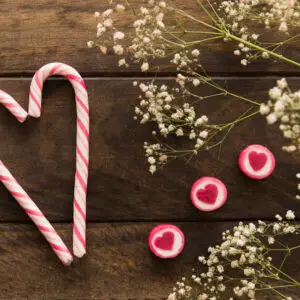 Red and white striped Candy Canes in the shape of a heart beside some heart candies and scrubby flowers